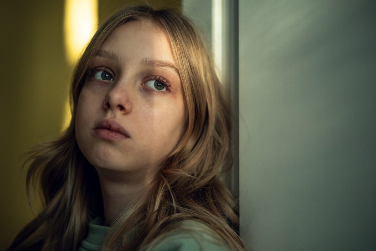 Sad girl with long blonde hair leaning against a wall in soft light