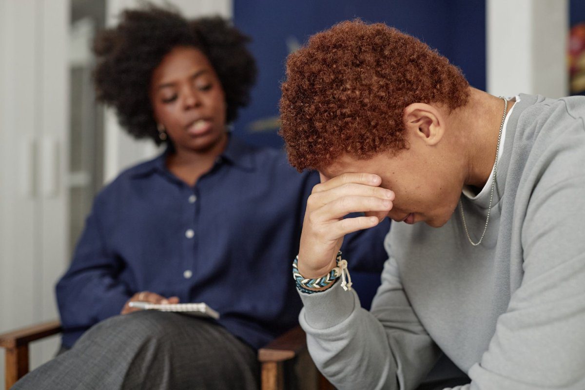 A person with their head in their hand sits while another person places a comforting hand on their shoulder