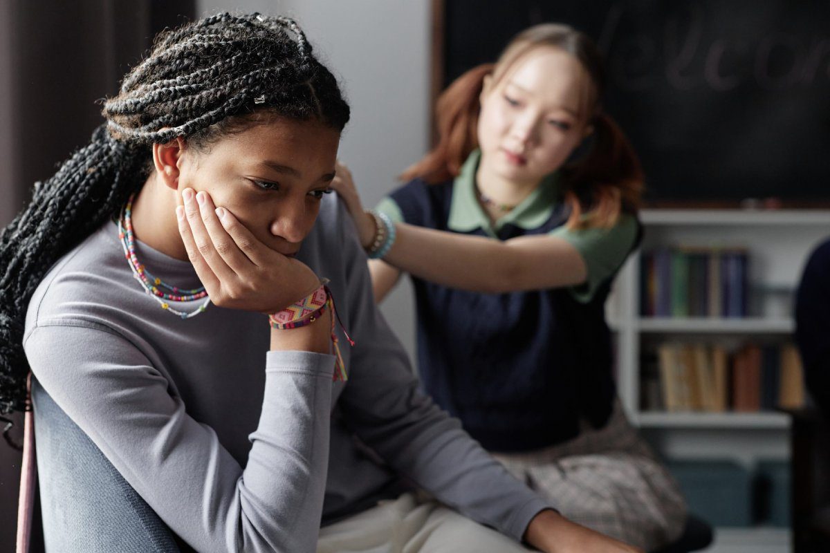 A young girl sitting on a chair, resting her chin on her hand, looking thoughtfully to the side